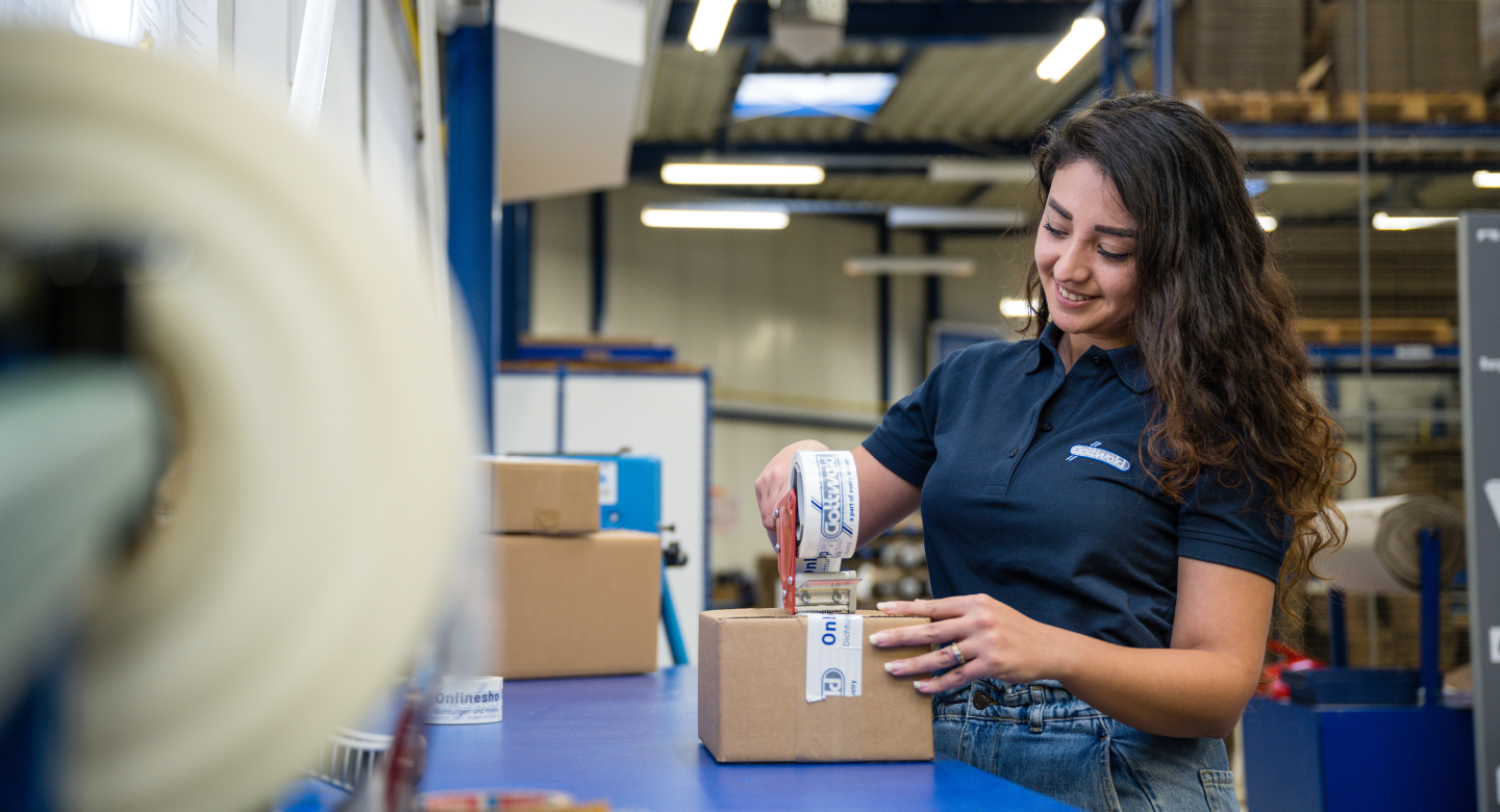 Eine Mitarbeiterin von Franz Gottwald verpackt in der Versandabteilung ein Paket mit bedrucktem Klebeband.