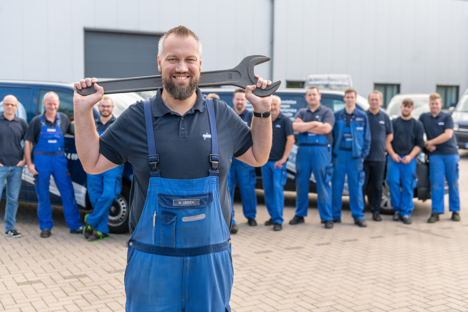 Servicetechniker von Franz Gottwald posieren vor Firmenfahrzeugen, ein Mitarbeiter hält einen großen Schraubenschlüssel über den Schultern.