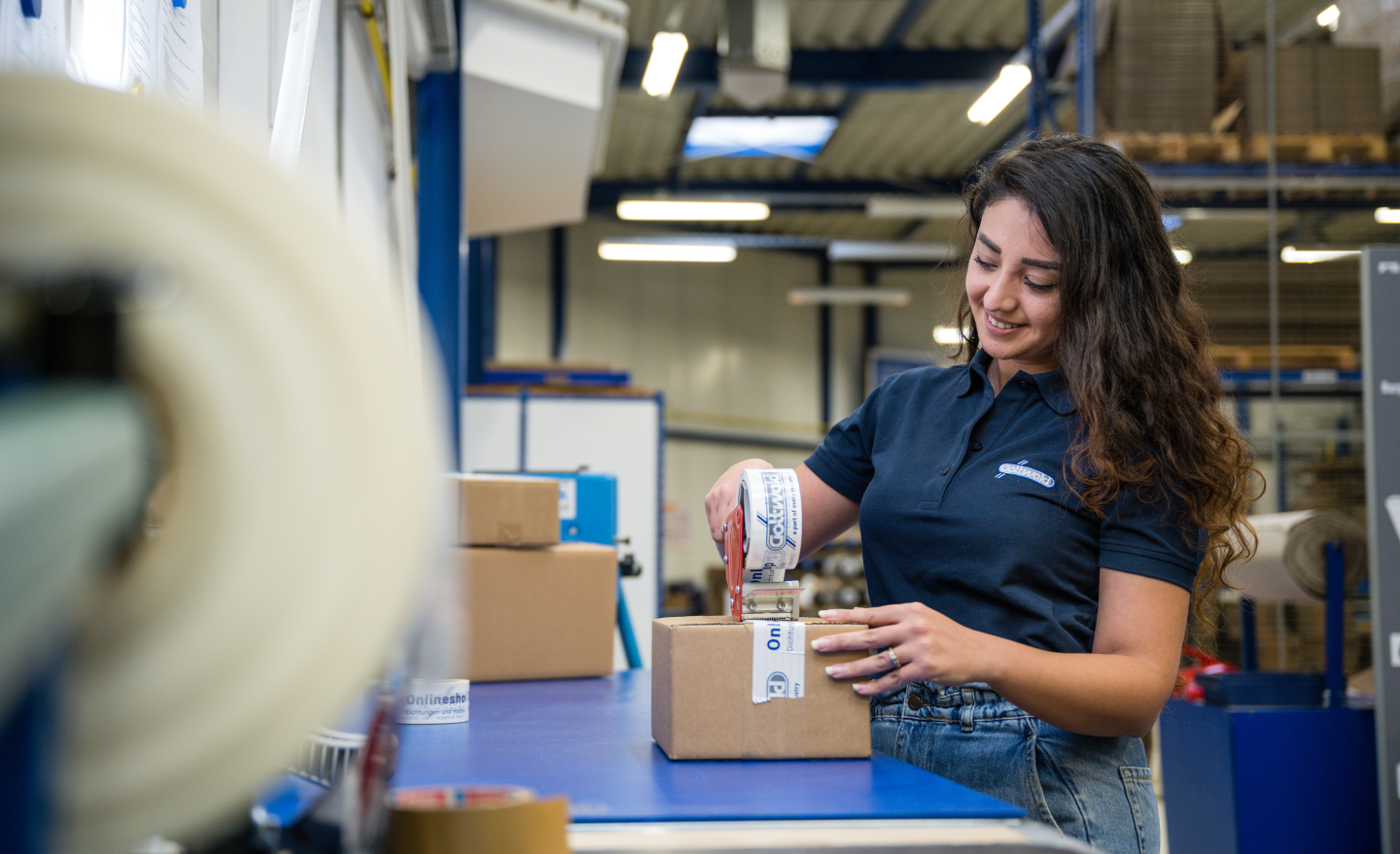 Eine Mitarbeiterin von Franz Gottwald verpackt ein Paket mit bedrucktem Klebeband.