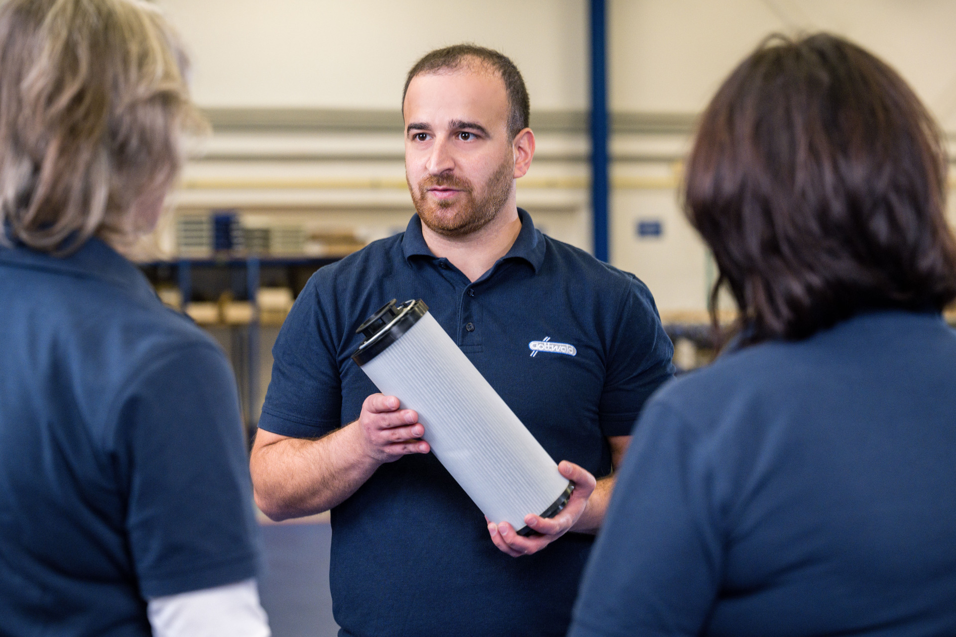 Mitarbeiter der Franz Gottwald GmbH + Co. KG erklärt zwei Kolleginnen ein großes Hydraulikfilterelement.