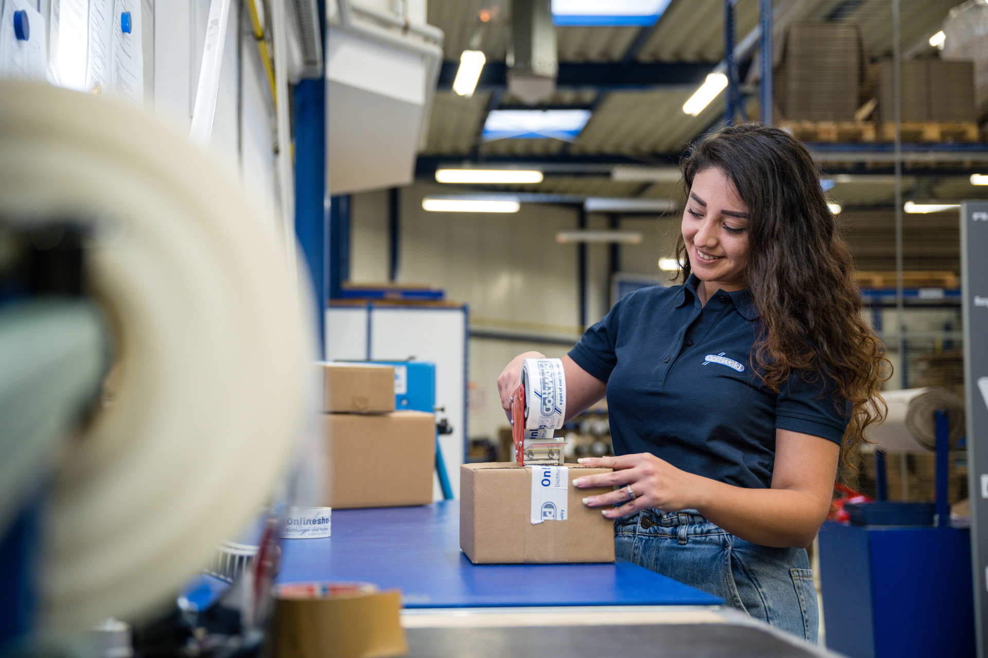 Mitarbeiterin der Franz Gottwald GmbH + Co. KG verpackt im Versandbereich ein Paket mit firmeneigenem Klebeband.