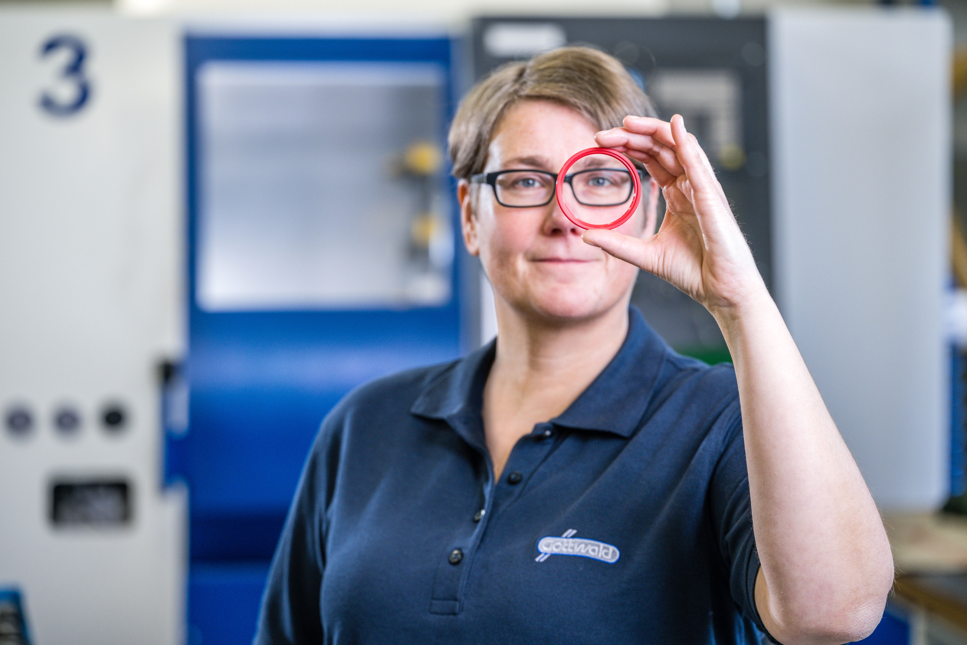 Eine Mitarbeiterin von Franz Gottwald blickt durch einen roten Dichtungsring.