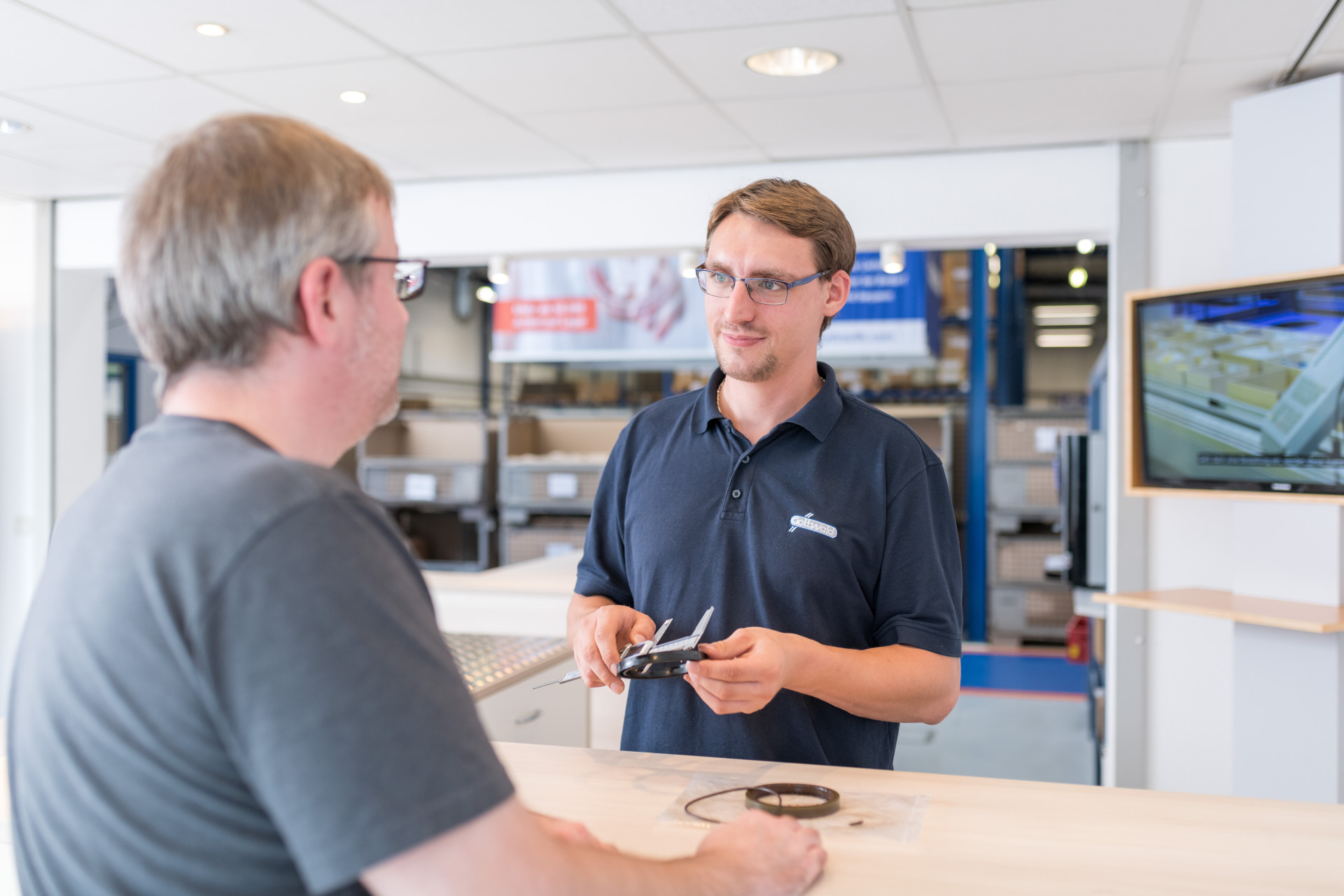Ein Mitarbeiter von Franz Gottwald berät einen Kunden am Tresen und hält eine Schieblehre in der Hand.