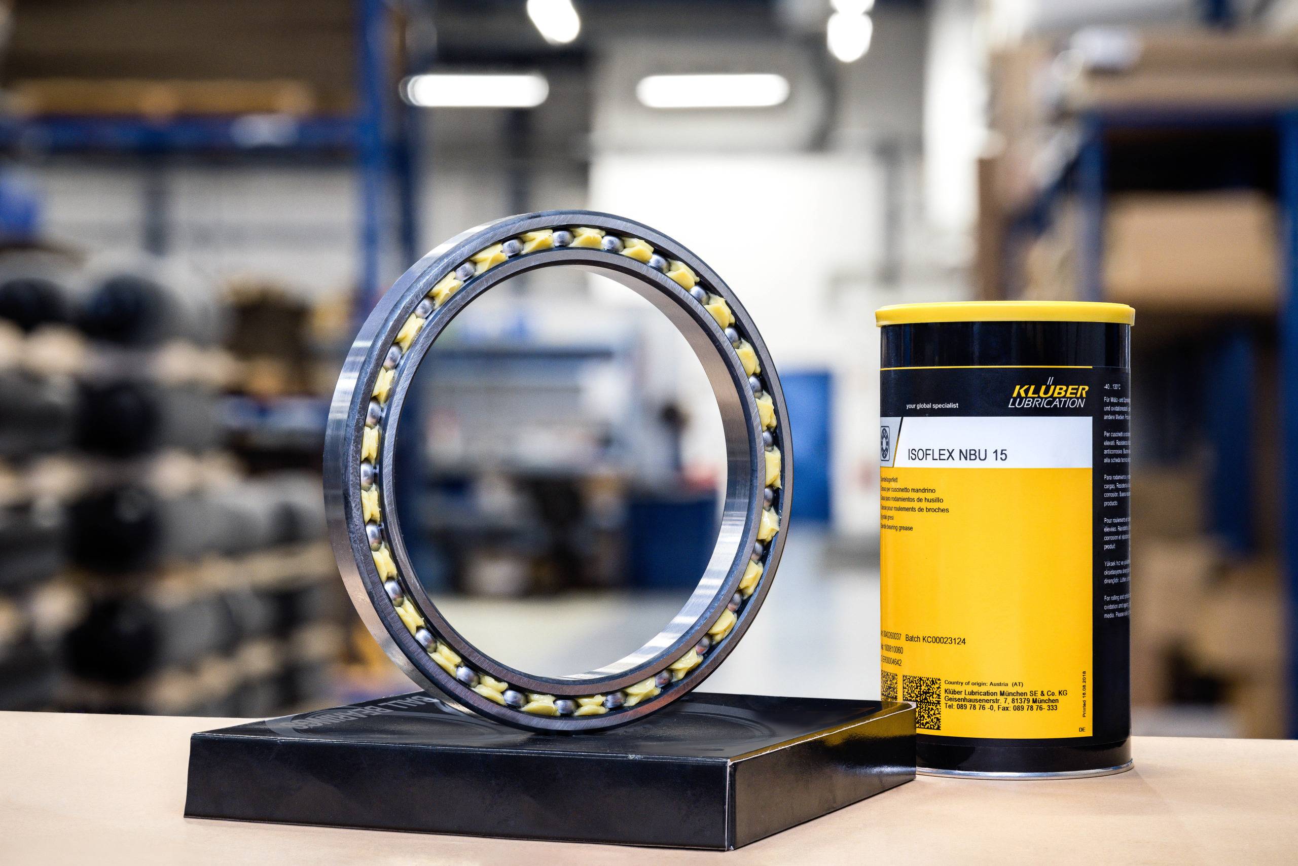 Ein Wälzlager steht auf einem Sockel neben einer Dose Klüber Lubrication Fett in einer Werkhalle.