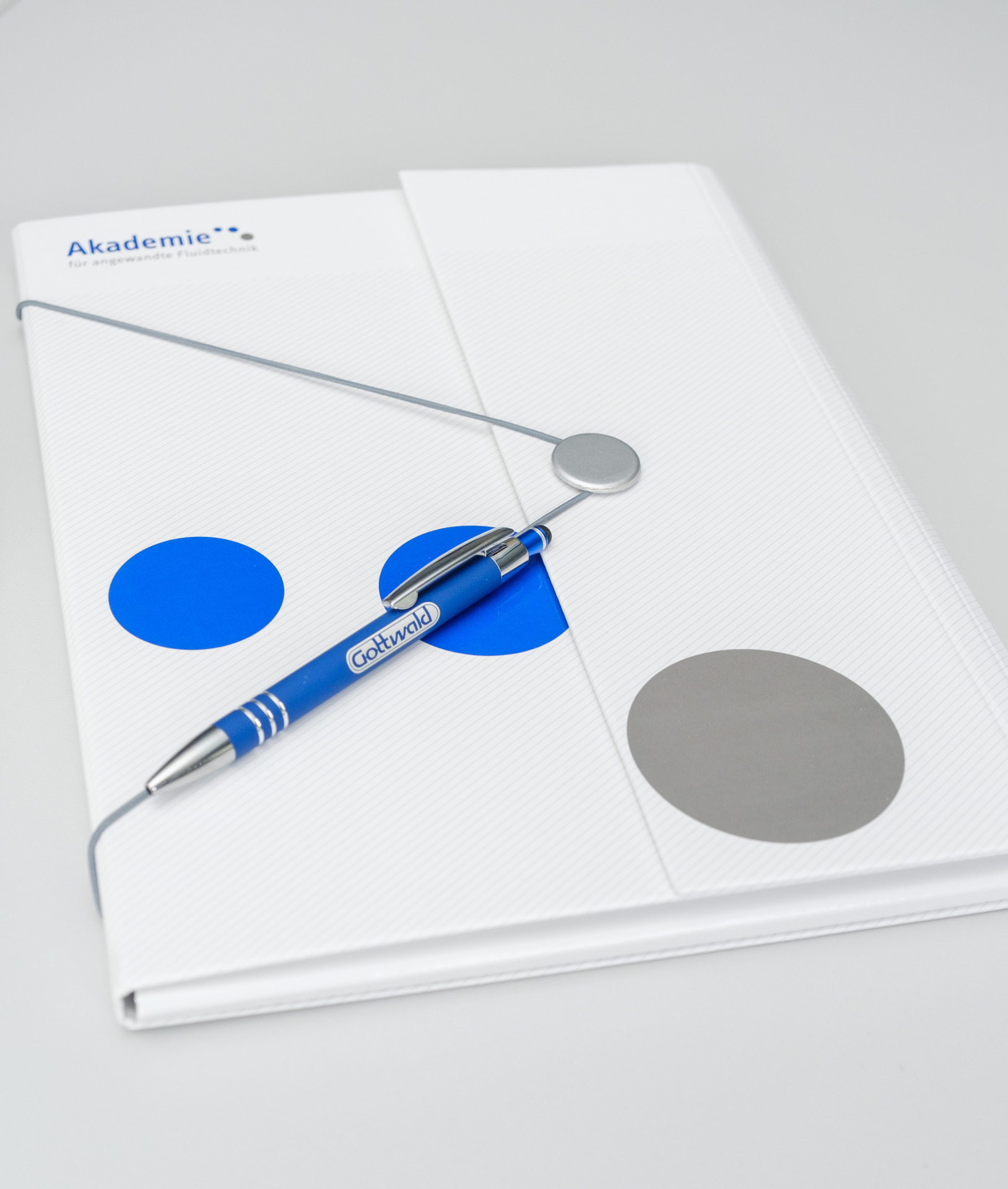 Ein Kugelschreiber mit Gottwald-Logo liegt auf einer weißen Mappe der „Akademie für angewandte Fluidtechnik“.
