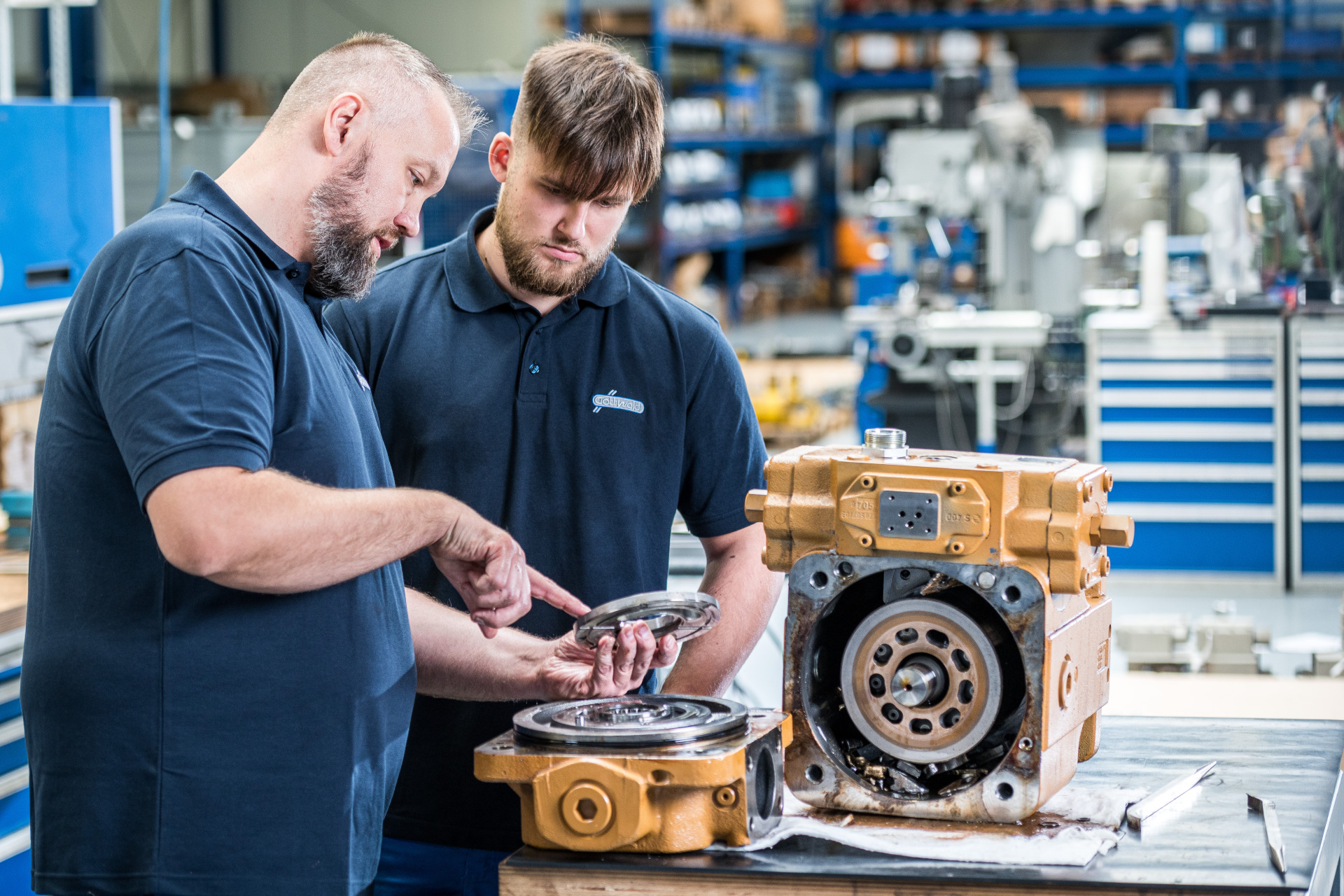 Zwei Mitarbeiter von Franz Gottwald begutachten ein Bauteil und besprechen Details an einem geöffneten Hydraulikaggregat.