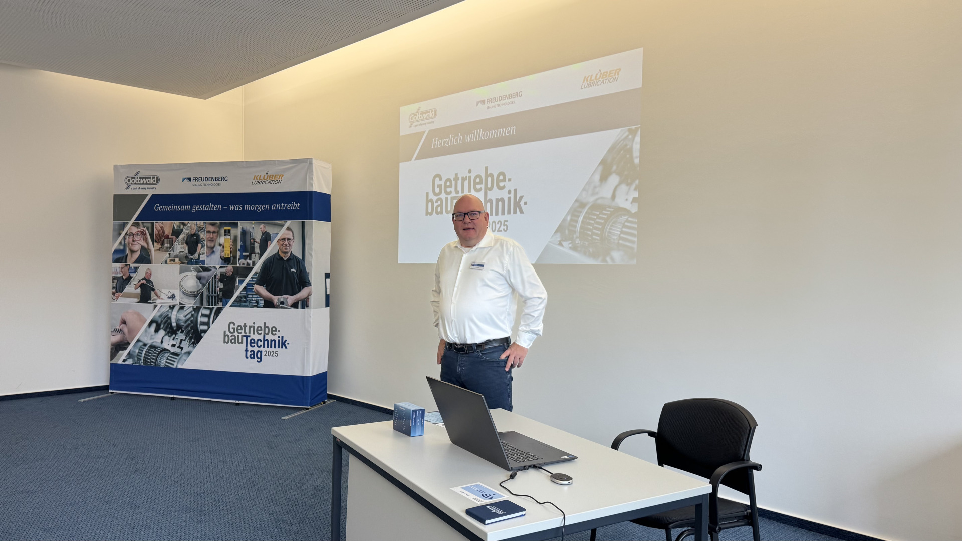 Ein Mitarbeiter von Franz Gottwald begrüßt Teilnehmende zum Getriebebau-Techniktag 2025 in einem Präsentationsraum.