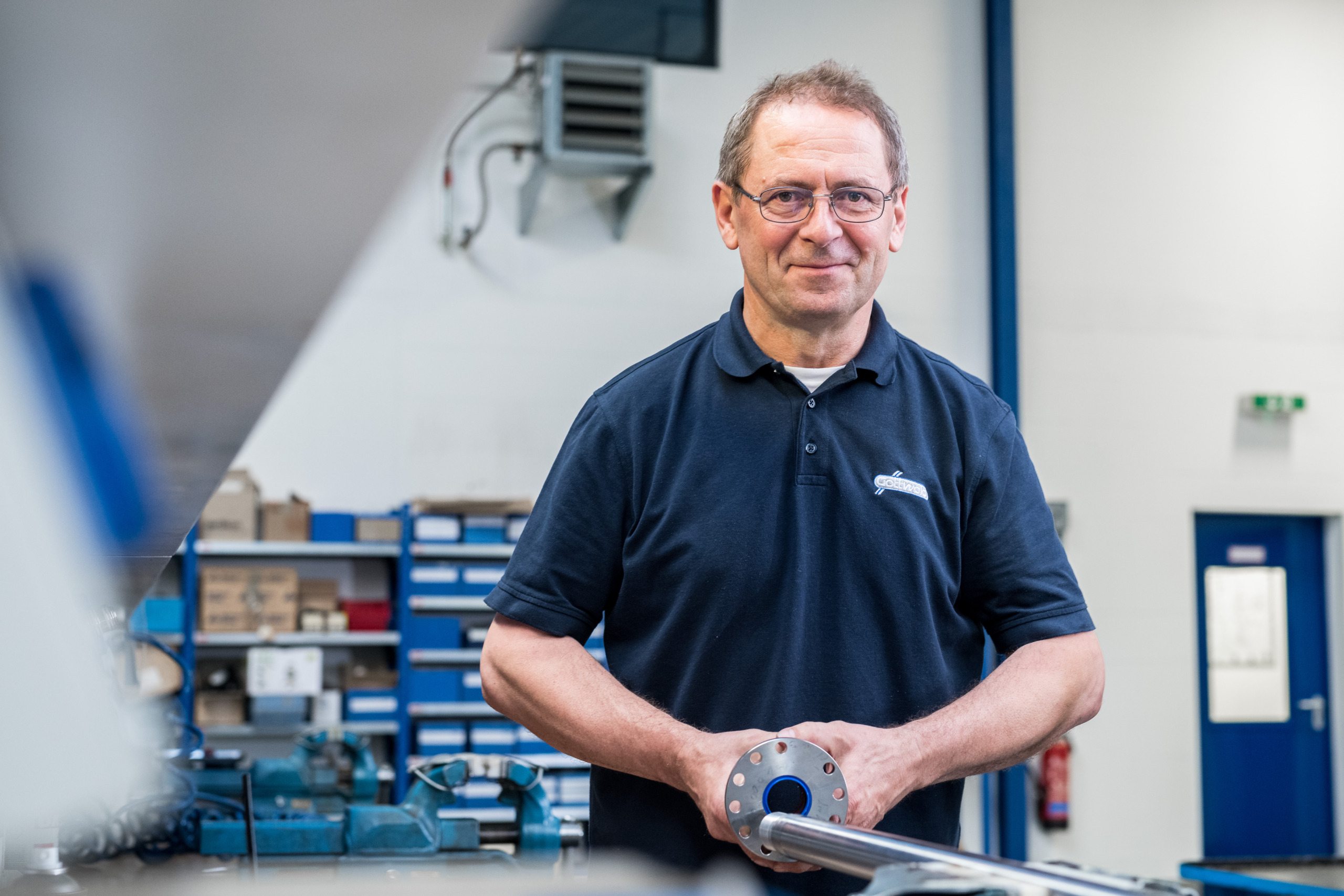 Hydrauliker von Franz Gottwald hält eine Kolbenstange mit Flansch in der Hydraulik-Werkstatt.